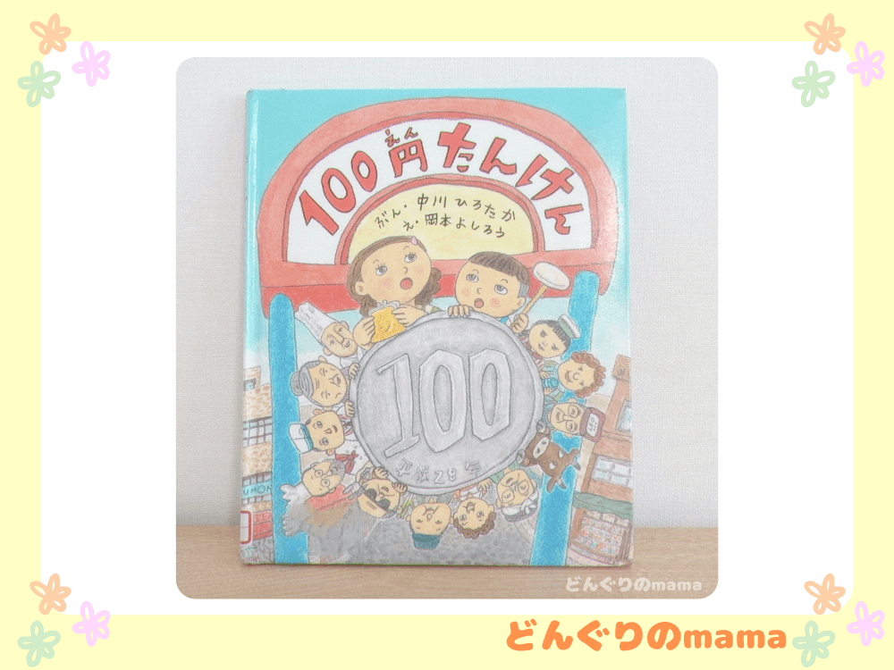絵本「100円たんけん」の表紙をデスク上で壁に立てかけて撮影した写真