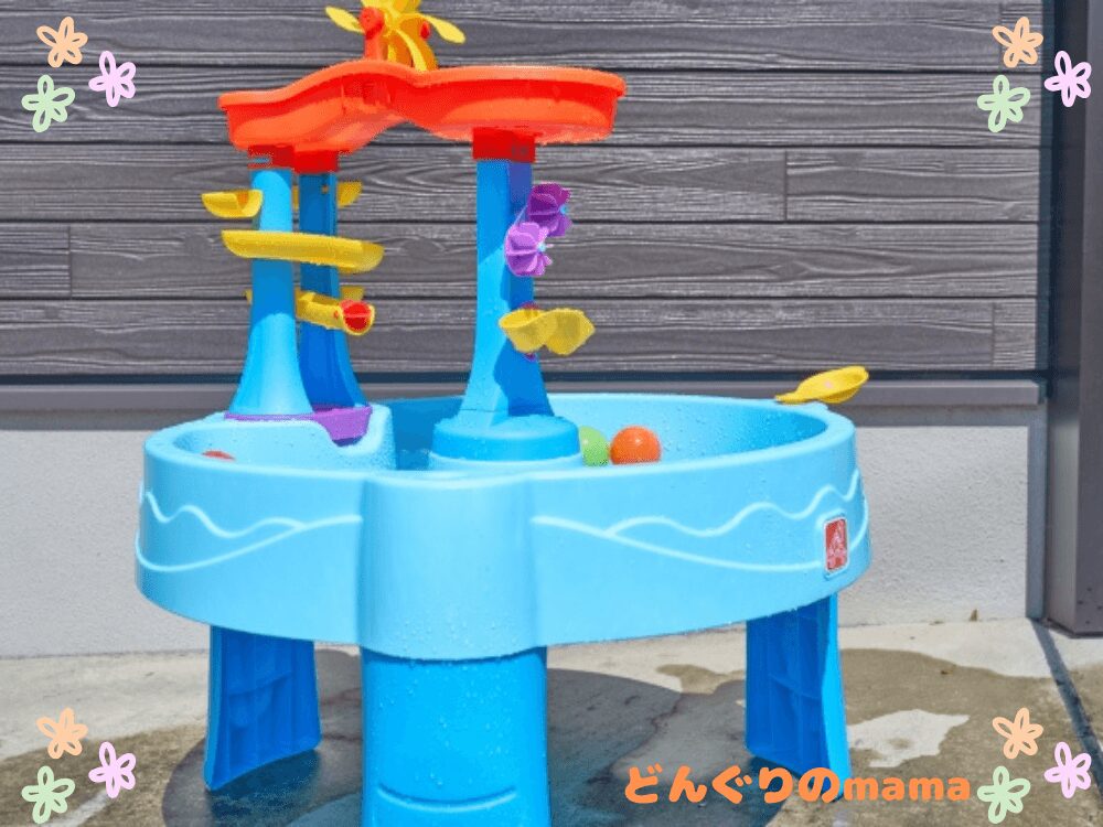 子どもがウォーターテーブルで水遊びを楽しんでいる様子。夏の公園遊びや屋外活動のイメージ。